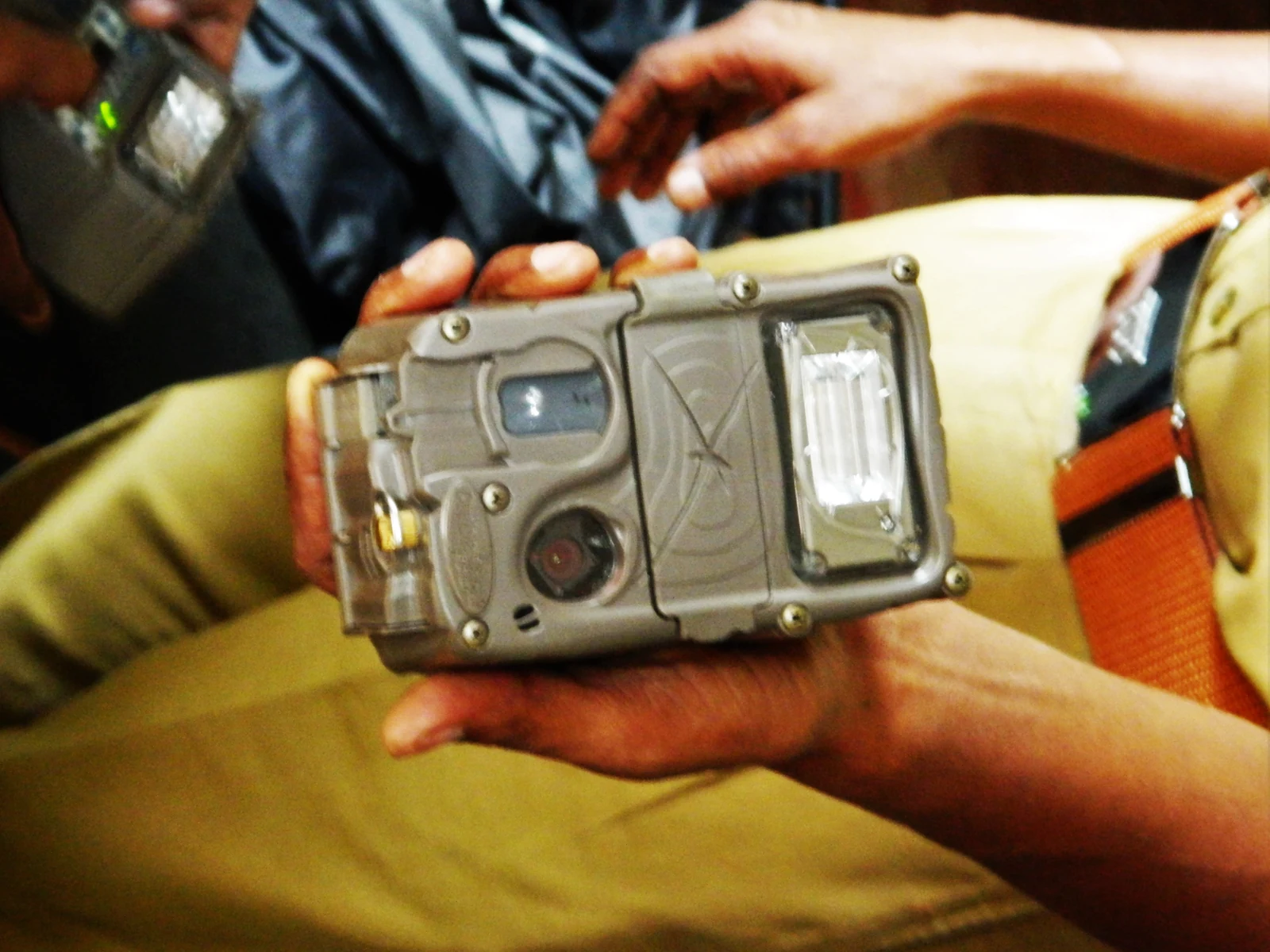 Hands holding a trail camera beside field equipment